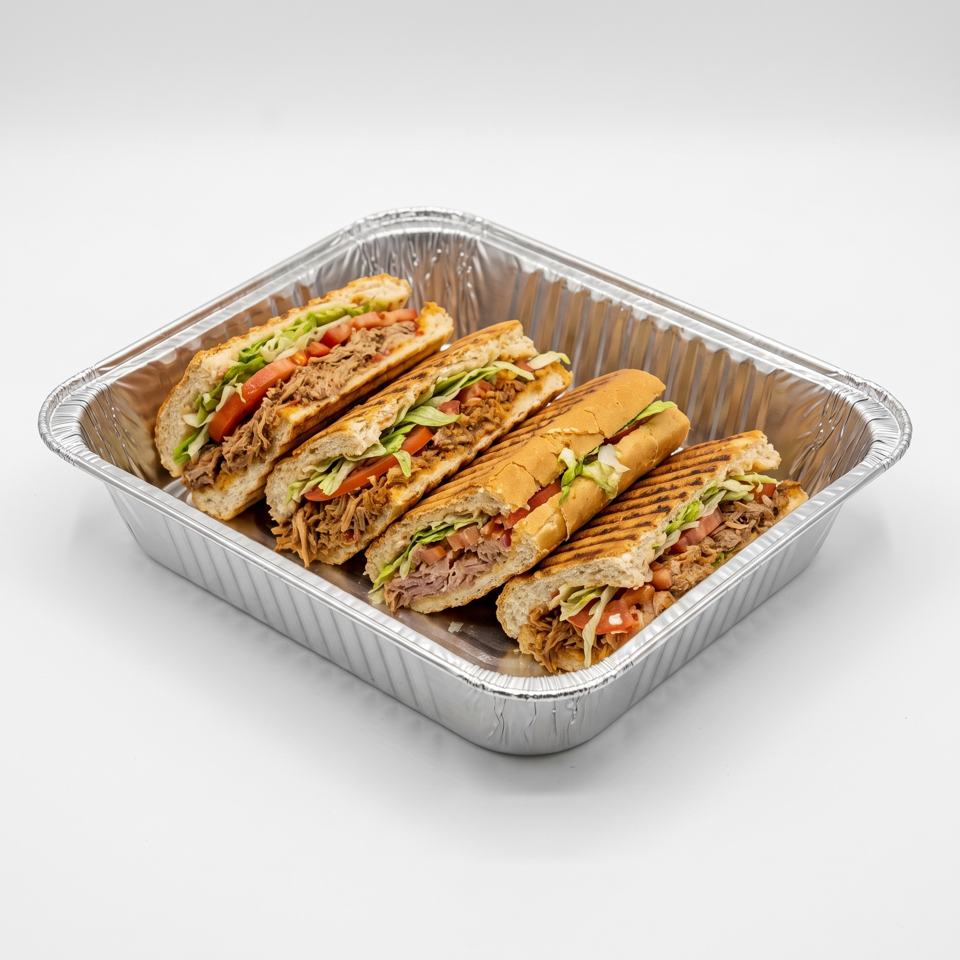 Aluminum tray filled with grilled meat sandwiches on pita and rolls, topped with lettuce and tomatoes.